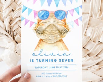 Peut inclure: Une invitation blanche avec une illustration à l'aquarelle d'un dragon barbu portant des lunettes de soleil roses. Le texte indique "Olivia a sept ans" avec les détails de l'événement ci-dessous. Une bannière de fanions bleus et roses décore le haut.