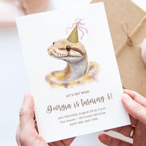 May include: Birthday invitation featuring a watercolor illustration of a snake wearing a gold party hat. The text reads "LET'S GET WILD! Georgia is turning 8!" with event details. The invitation is held by a person.