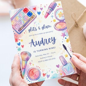 May include: A watercolor invitation for a makeup spa party. The invitation features makeup illustrations, including an eyeshadow palette, lipstick, and blush. The text reads "glitz & glam" and "Audrey is turning nine!"