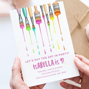 Op de afbeelding: Witte uitnodigingskaart met kleurrijke penselen en druipende verf. Tekst luidt "LET'S PUT THE ART IN PARTY! ISABELLA is 9!" met evenementdetails. De kaart wordt door handen vastgehouden.