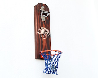 Puede incluir: Abrebotellas de madera con un aro de baloncesto y una red. El abrebotellas tiene el logotipo de los New York Knicks y un abrebotellas plateado.