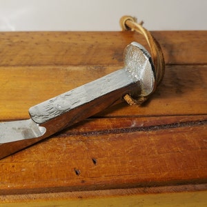 May include: A silver bottle opener shaped like a nail with a leather loop. The opener is sitting on a wooden surface.