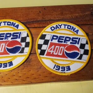 May include: Two round white embroidered patches with a yellow border. The patches feature a checkered flag, the text "DAYTONA PEPSI 400 1993", and a red, white, and blue Pepsi logo.