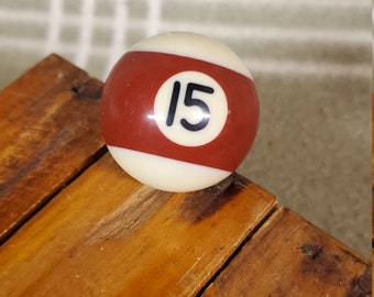May include: A red and white billiard ball with the number 15 printed in black on it.