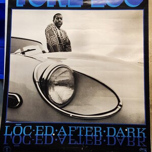 Op de afbeelding: Een zwart-wit poster met een man in een gepatroneerde trui die voor een witte auto staat. De poster heeft de tekst "TONE LOC" in blauwe letters en "LOC-ED: AFTER: DARK" in blauwe letters.