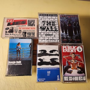 以下が含まれることがあります： 「GN'R Lies」、「The Wall」、「Rest In Peace」、「Sweet Forgiveness」、「U2 Boy」、「Public Enemy Muse Sick-N-Hour Mess Age」など、8 本のカセットテープのコレクションです。