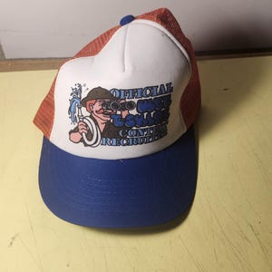 May include: A white foam front trucker hat with an orange mesh back and a blue brim. The front features a graphic of a person with a moustache holding binoculars and a water hose, with the text "OFFICIAL WET T-SHIRT CONTEST RECRUITER" in blue.