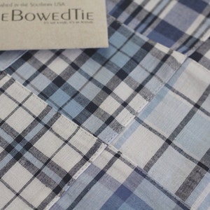 May include: Close-up of a blue and white plaid fabric with a sewn seam. The fabric has a subtle texture and a slightly faded appearance.