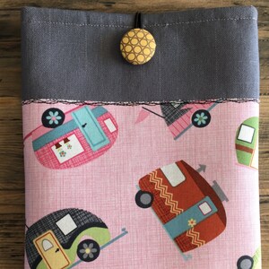 May include: A gray fabric pouch with a pink fabric lining featuring a repeating pattern of colorful vintage camper vans. The pouch has a green and white ribbon trim and a yellow button closure.