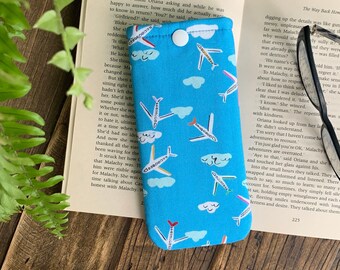 May include: A blue and white eyeglass case with a pattern of airplanes and clouds. The case has a button closure.