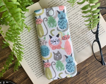 May include: White fabric eyeglasses case with a colorful pattern of cats. The cats are in various poses and have different colored fur. The case has a button closure.