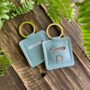 May include: Two light blue leather keyrings with gold rings. One keyring has a coin pocket and the other has a letter "D" embossed on the front.