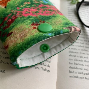 Puede incluir: Un estuche para gafas de tela verde y blanca con estampado floral y dos cierres de presi&oacute;n verdes.