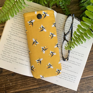 May include: A yellow fabric glasses case with a repeating pattern of black and yellow bees. The case has a black button closure.