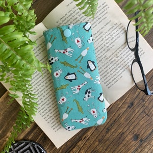 Peut inclure: Un étui à lunettes bleu clair avec un motif fantaisiste de girafes, pingouins, vaches et alligators. L'étui est doté d'une fermeture à bouton et est fait de tissu.