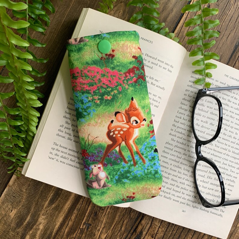 Puede incluir: Un estuche para gafas de tela verde, rosa y azul con cierre de presi&oacute;n. El estuche presenta una imagen de dibujos animados de Bambi y Tambor de la pel&iacute;cula de Disney Bambi.
