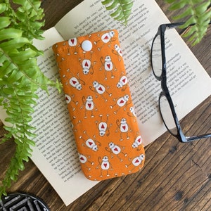 Peut inclure: Étui à lunettes en tissu orange avec un motif répété de singes blancs avec des cœurs rouges. L'étui est doté d'une fermeture à bouton.
