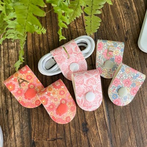 May include: Five colorful cable organizers with floral patterns and a button closure. The organizers are labeled with the letters A, E, and S.