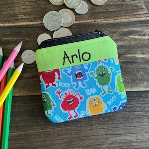 May include: A small zippered pouch with a green and blue monster print. The pouch has a lime green flap with the name "Arlo" written in black.