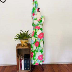 May include: A sleeveless maxi dress with a V-neckline and a floral print in shades of pink, blue, green, and white. The dress is on a mannequin and is displayed against a white wall.