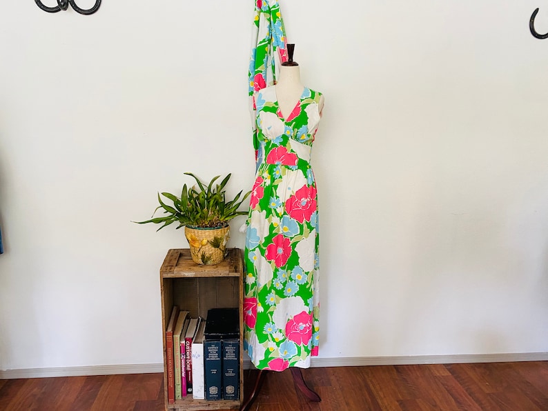 May include: A sleeveless maxi dress with a V-neckline and a floral print in shades of pink, blue, green, and white. The dress is on a mannequin and is displayed against a white wall.