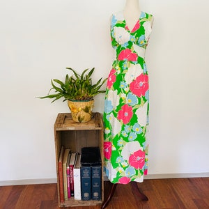 May include: A sleeveless maxi dress with a V-neckline and a floral print in shades of pink, blue, and green on a white background. The dress is on a mannequin and is displayed against a white wall.