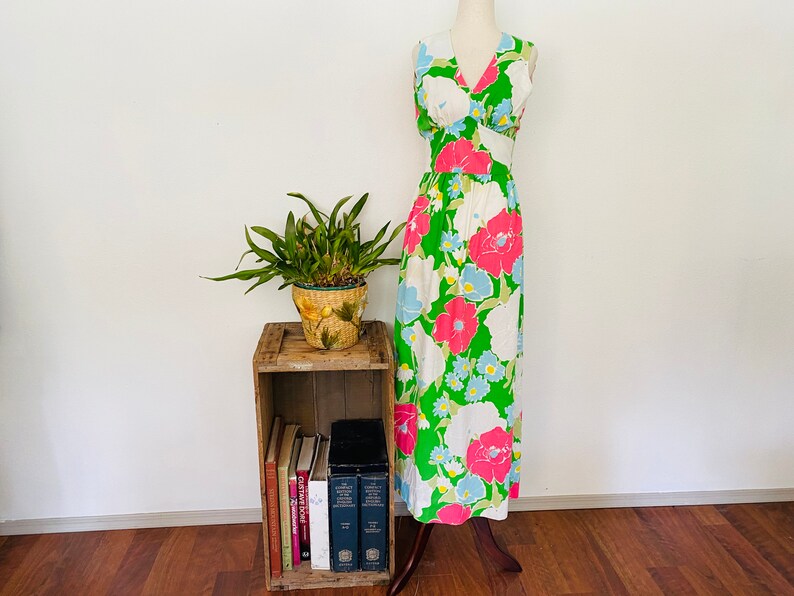 May include: A sleeveless maxi dress with a V-neckline and a floral print in shades of pink, blue, and green on a white background. The dress is on a mannequin and is displayed against a white wall.