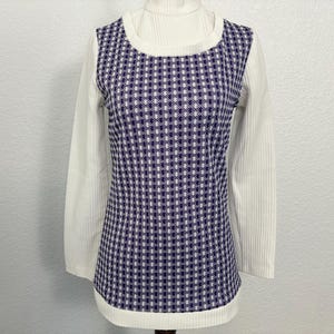 May include: A vintage-style top with a white ribbed turtleneck and long sleeves. It features a sleeveless overlay with a blue and white checkered pattern. The design has a classic, retro aesthetic.