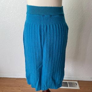 May include: A turquoise blue, ribbed knit skirt. The skirt has a high, ribbed waistband and a knee-length hem. The fabric has a vertical ribbed texture. The skirt is displayed on a mannequin.