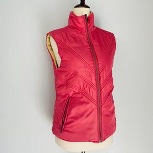 May include: A red quilted vest with a zipper closure and a stand-up collar.