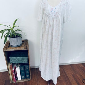 May include: A vintage white nightgown with short sleeves and a floral pattern. The gown features a detailed bodice with delicate embroidery and a flowing, floor-length design. The fabric appears lightweight and comfortable, perfect for sleepwear.