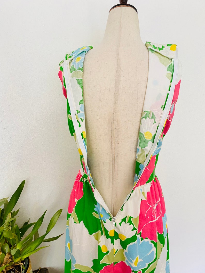 May include: A white dress with a green, pink, and blue floral print. The dress has a sleeveless design and a zipper down the back.