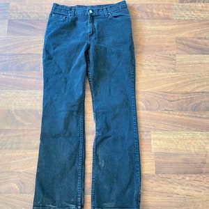 May include: Dark wash denim jeans with a classic five-pocket design. The jeans have a straight leg fit and a button and zip closure. The jeans are laid flat on a wooden surface.