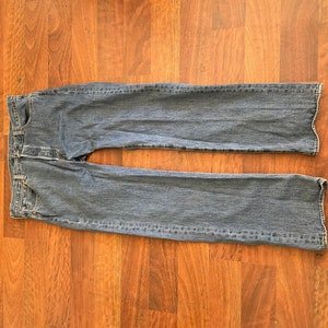 May include: A pair of blue denim jeans laid flat on a wooden floor.