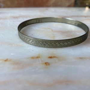 May include: A silver bangle bracelet with a geometric pattern.