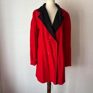 May include: A double-breasted red coat with a black collar and lapels. The coat has long sleeves and a button closure. The coat is displayed on a mannequin.
