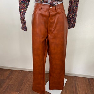May include: Brown faux leather trousers with a straight leg fit. The trousers have a zip fly and button fastening.