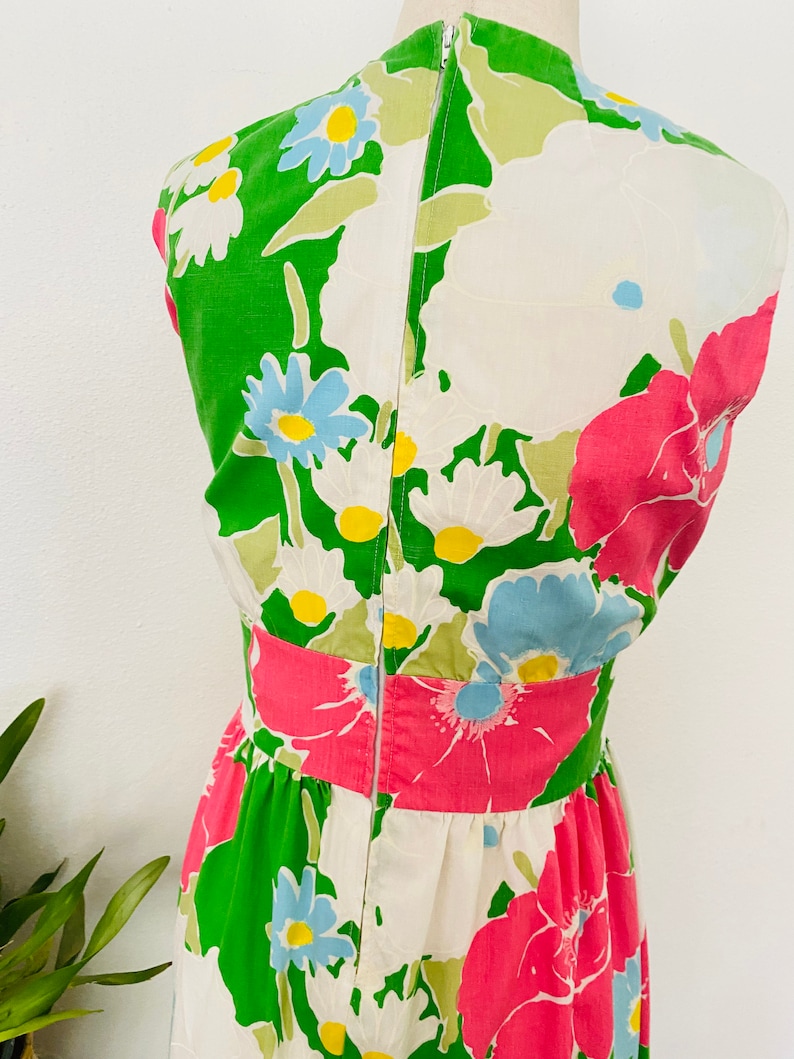 May include: A white dress with a green, pink, and blue floral print. The dress has a sleeveless design and a back zipper closure.