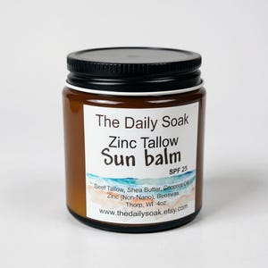 May include: A brown glass jar with a black lid, labeled "The Daily Soak Zinc Tallow Sun balm SPF 25." The label lists ingredients like beef tallow, shea butter, and beeswax. The jar is 4oz.
