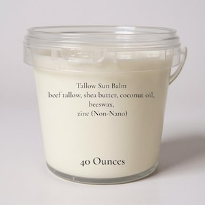 May include: A clear plastic container filled with a creamy, off-white balm. The label reads "Tallow Sun Balm" and lists ingredients: beef tallow, shea butter, coconut oil, beeswax, and zinc (Non-Nano). The container holds 40 ounces.