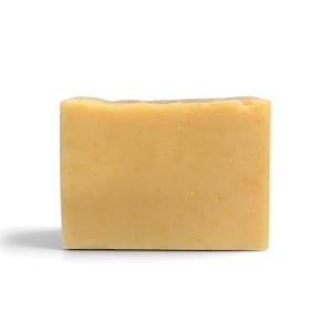 May include: A rectangular bar of solid soap with a smooth, matte finish in a light golden-yellow hue. The soap features a uniform, opaque appearance with subtle variations in color throughout the surface, presenting a clean and simple block shape.