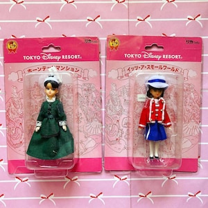 May include: Two Tokyo Disney Resort dolls in packaging. One doll wears a green dress and white bonnet. The other doll wears a red jacket, blue skirt, and white hat. The packaging reads "TOKYO DISNEY RESORT" and Japanese text.