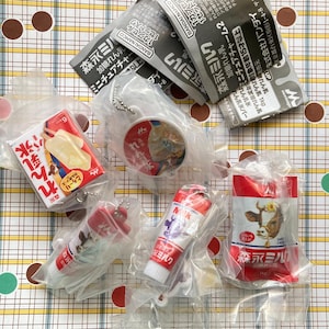 May include: A collection of miniature Japanese food-themed keychains and packaged items. The items include a red and white popsicle, a keychain with a round image, and several packages of milk products. The packaging features Japanese text and cartoon illustrations.
