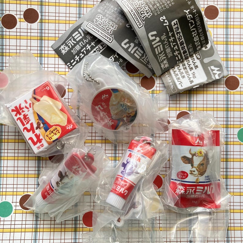 May include: A collection of miniature Japanese food-themed keychains and packaged items. The items include a red and white popsicle, a keychain with a round image, and several packages of milk products. The packaging features Japanese text and cartoon illustrations.