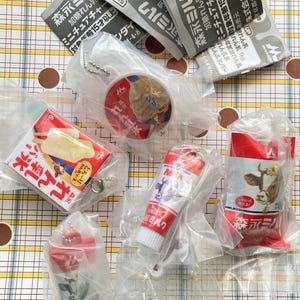 May include: A collection of miniature Japanese food items, including milk cartons, ice cream bars, and a tube of milk, all in their original packaging. The items are red, white, and blue, and some have Japanese text.