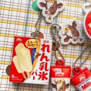 May include: A collection of Japanese-themed keychains and a small box of ice cream. The keychains feature a cow with a flower crown and a bell. The ice cream box is red and white with Japanese text and images of ice cream.