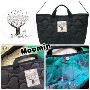 May include: A black quilted tote bag featuring a rectangular patch with a Moomin illustration of a tree and characters. The interior is lined with a green and blue patterned fabric and includes a silver-toned metal snap button closure.