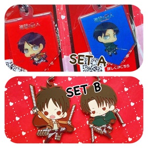 Puede incluir: Dos juegos de llaveros de personajes de Ataque a los Titanes. El set A presenta una tarjeta azul y roja con un personaje chibi en cada una. El set B presenta dos personajes chibi marrones con espadas.