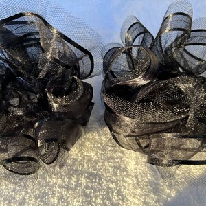 May include: Two black tulle bows with a shimmery finish. The bows are made of a soft, delicate material and are perfect for adding a touch of elegance to any occasion.