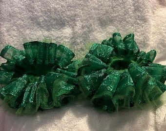 May include: Two green tulle hair bows with glitter accents. The bows are ruffled and have a shamrock pattern.
